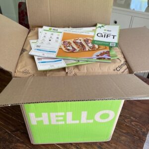 An open HelloFresh meal kit delivery with recipe cards on top of an insulated divider in a cardboard box