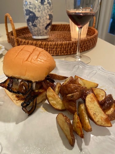 Plated Blue Apron burger with roasted potatoes and a glass of red wine.